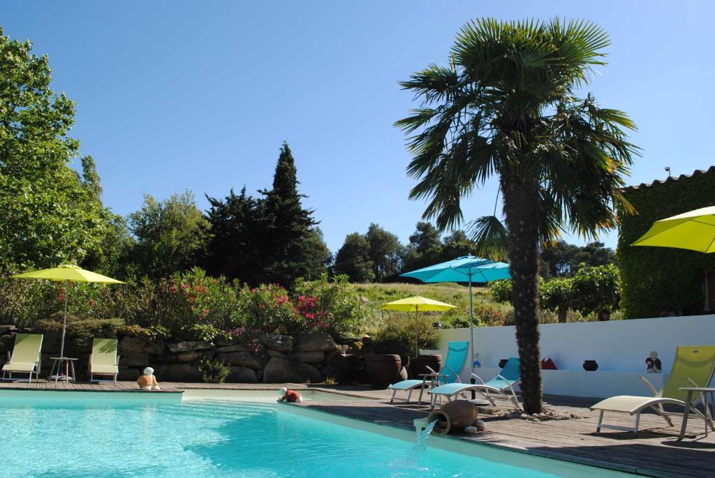 a swimming pool with chairs and umbrellas and a palm tree at Chambres d'hôtes & Spa le Relais de la Cavayere in Carcassonne