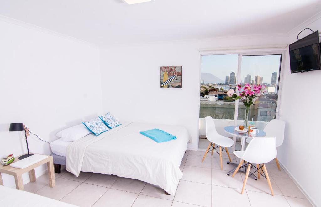 Playa Hotel Stay Work & Play Cavancha في إكيكي: غرفة نوم بيضاء بسرير وطاولة ونافذة