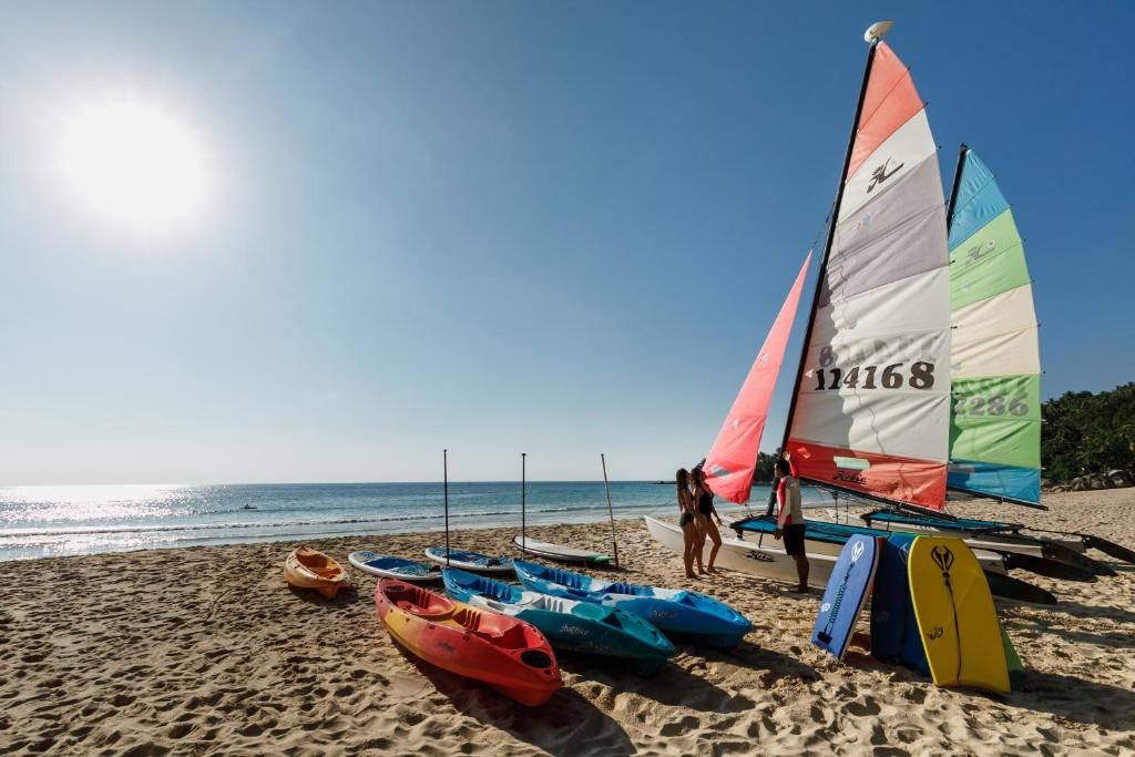 a group of kayaks on a beach with a sailboat at The Surin Phuket in Surin Beach