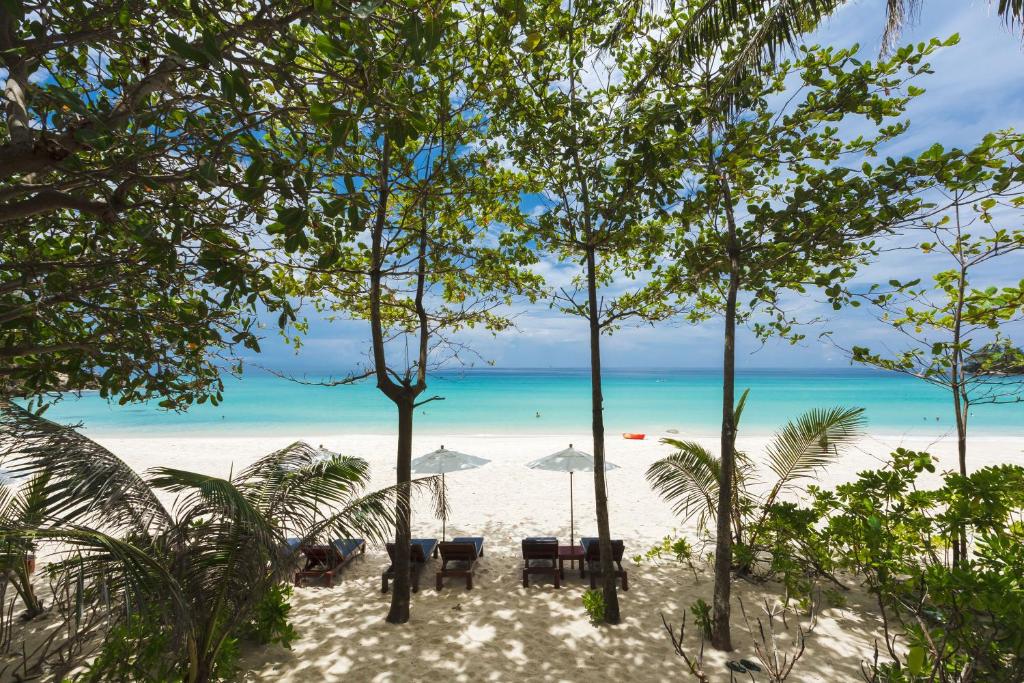 a beach with chairs and umbrellas and the ocean at The Surin Phuket in Surin Beach