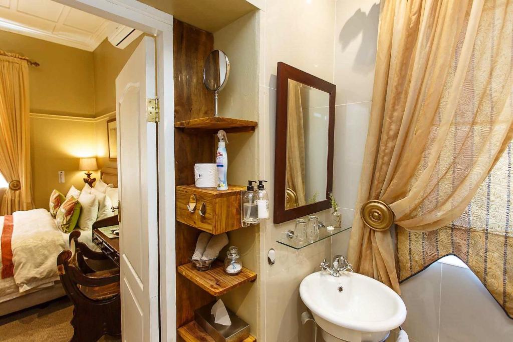 a bathroom with a sink and a mirror and a bed at Riverside Guest Lodge in Oudtshoorn