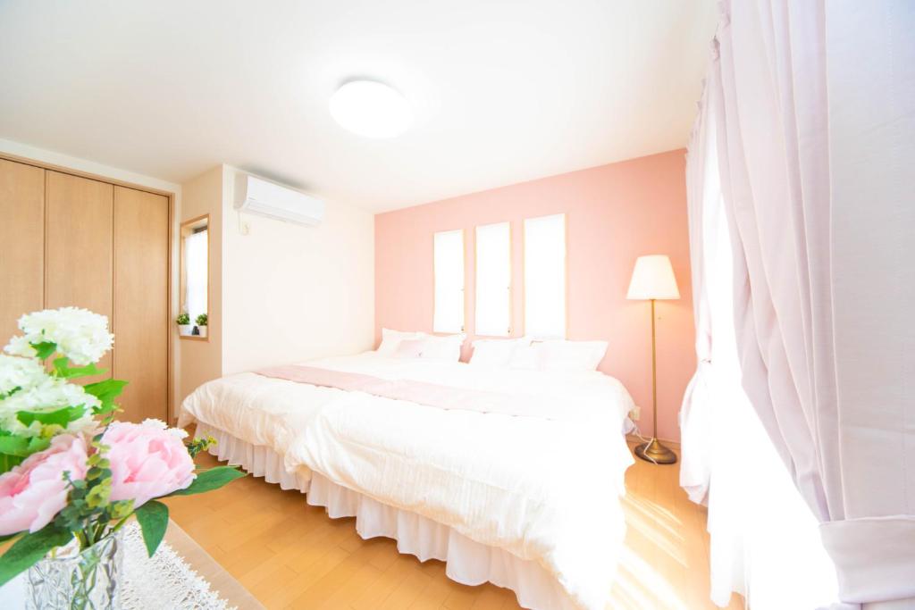 a white bedroom with a large white bed and flowers at Park side Villa Izumi Komoike in Izumi
