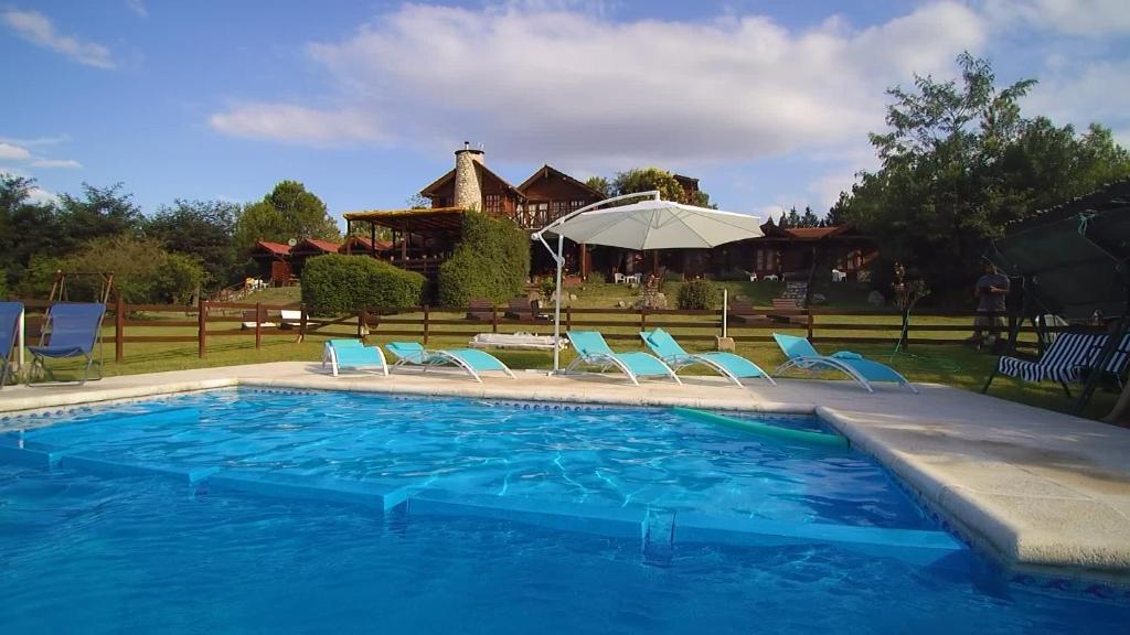 una piscina con sillas, una sombrilla y una casa en Posada La Ensenada en Villa Yacanto