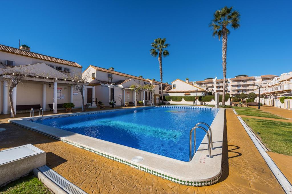 a swimming pool in front of a house with palm trees at Aldeas De Aguamarina Cabo Roig in Orihuela Costa