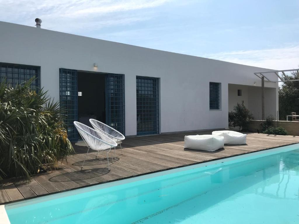 uma piscina com duas cadeiras brancas ao lado de uma casa em casa zabbara em Balestrate