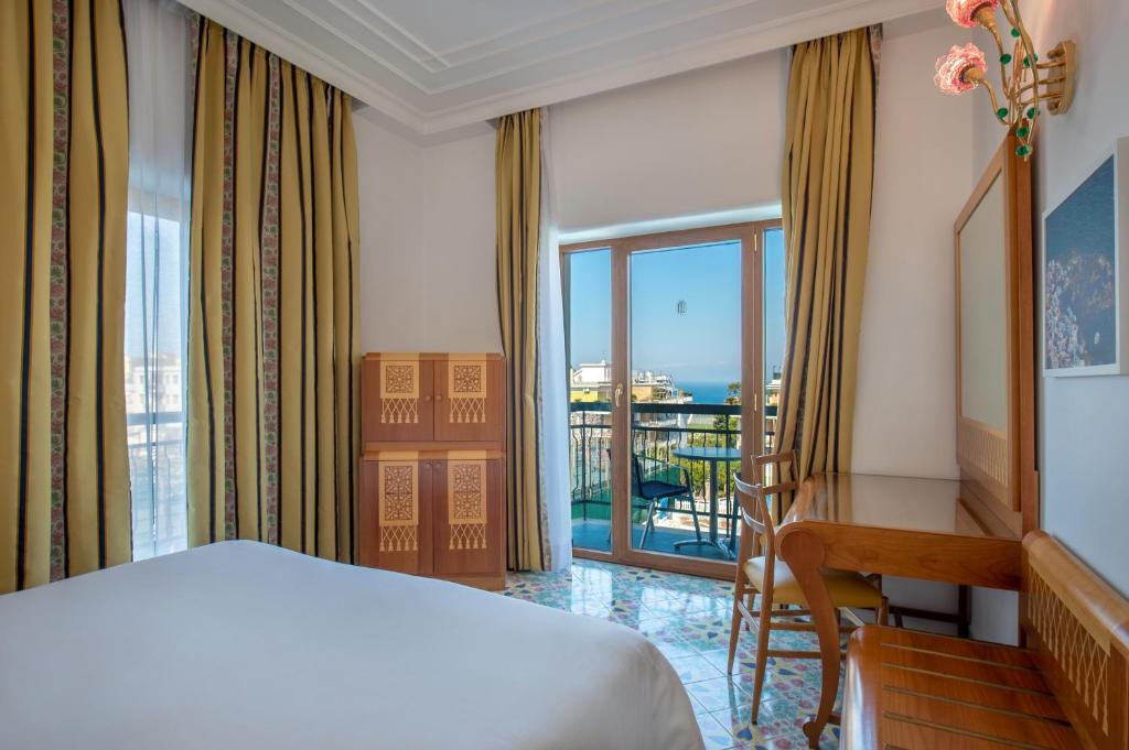 a bedroom with a bed and a desk and a balcony at Grand Hotel Flora in Sorrento