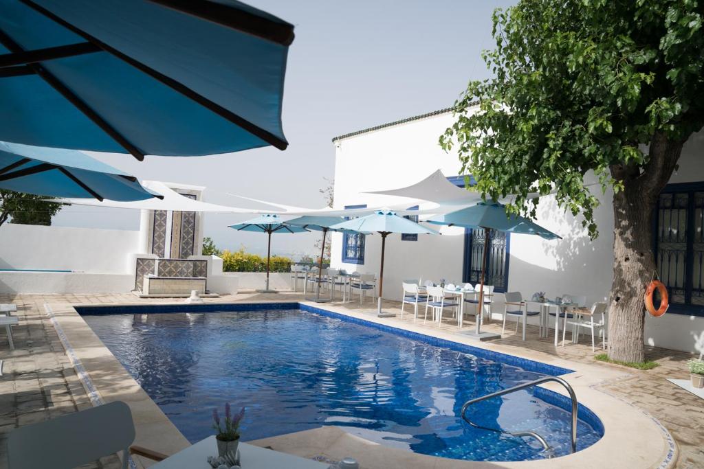 a swimming pool with blue umbrellas and tables and chairs at Dar Said in Sidi Bou Saïd