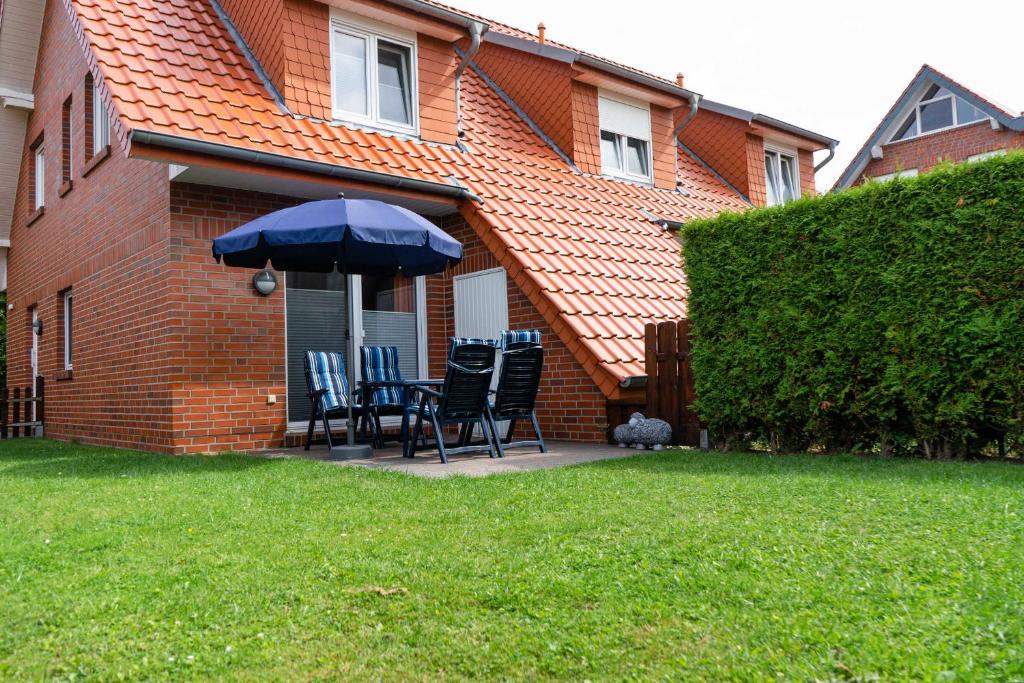 une terrasse avec des chaises et un parasol en face d'une maison dans l'établissement Ferienhaus Strandperle, à Horumersiel