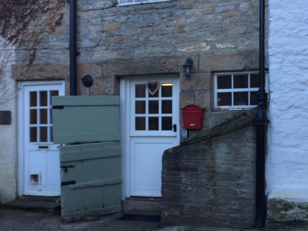a stone building with a white door and two windows at 'Stokoe Cottage' in Alston