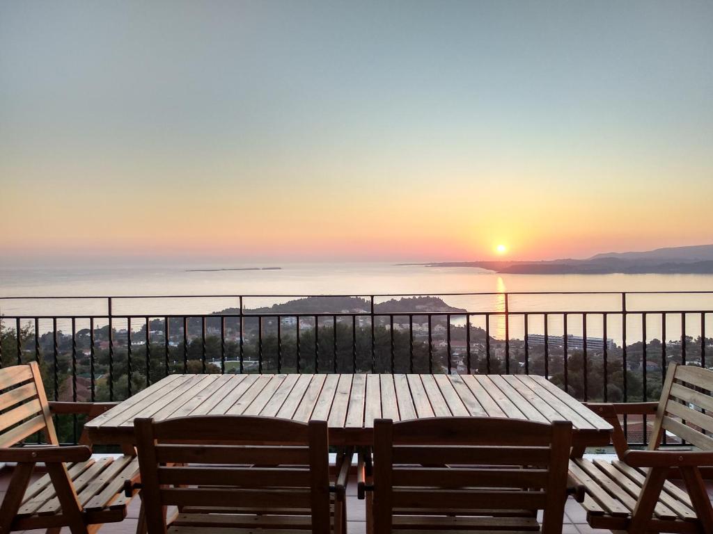 a wooden table and chairs on a balcony with a sunset at Greg's apartment in Argostoli