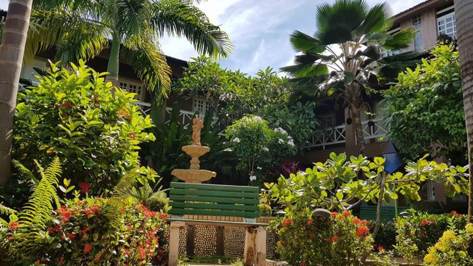 un banco verde en un jardín con una fuente en Pousada Porto dos Corais, en Maragogi