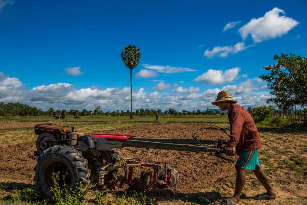 Um homem está a puxar um arado com um tractor. em Chansor Community Homestay 17 em Phumĭ Trach Pôk (2)