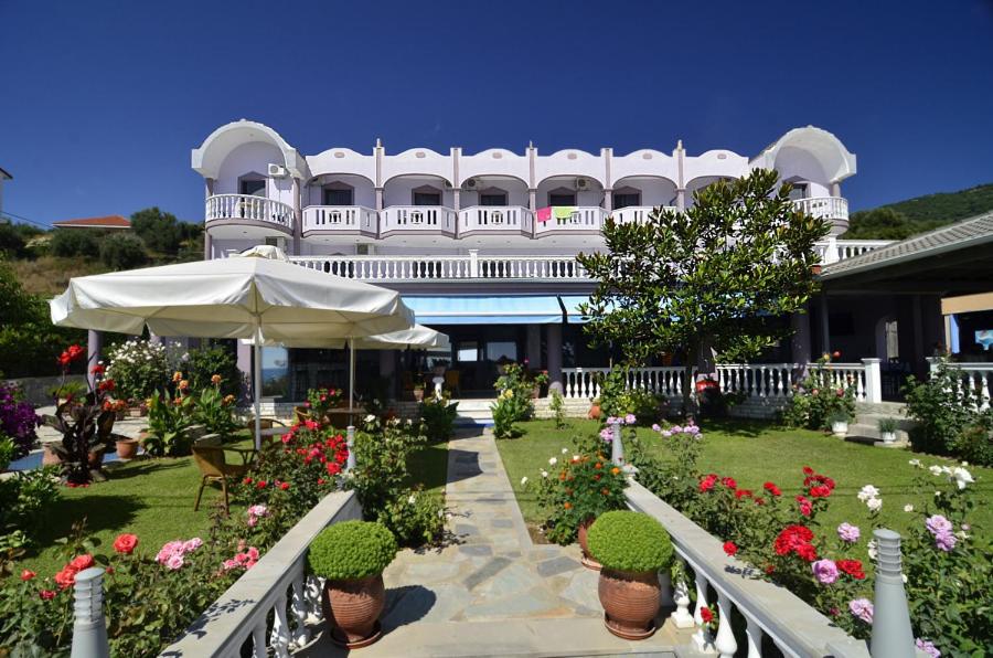 a building with a garden with flowers and an umbrella at Hotel Olympiada in Vráchos