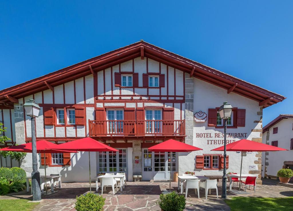 un edificio con mesas y sombrillas rojas delante de él en Hôtel Ithurria - Teritoria en Aïnhoa