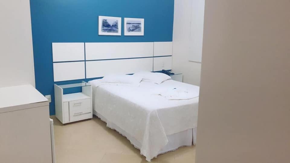 1 dormitorio con cama blanca y pared azul en Hotel Capri, en Nova Santa Medianeira