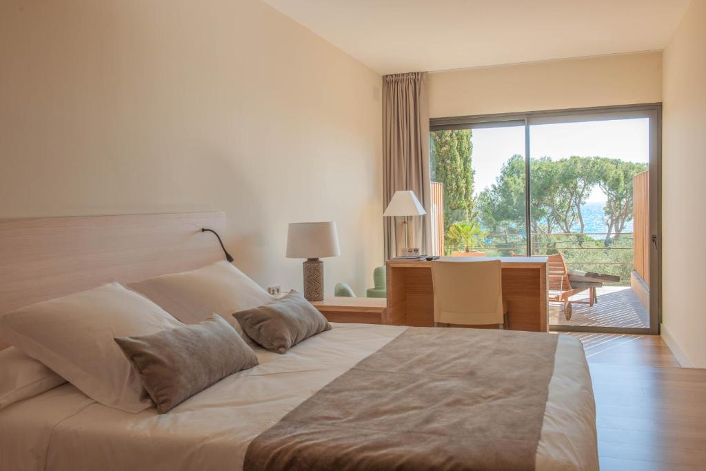 een slaapkamer met een groot bed en een bureau met een raam bij L'Aixart Aiguablava Hotel in Begur