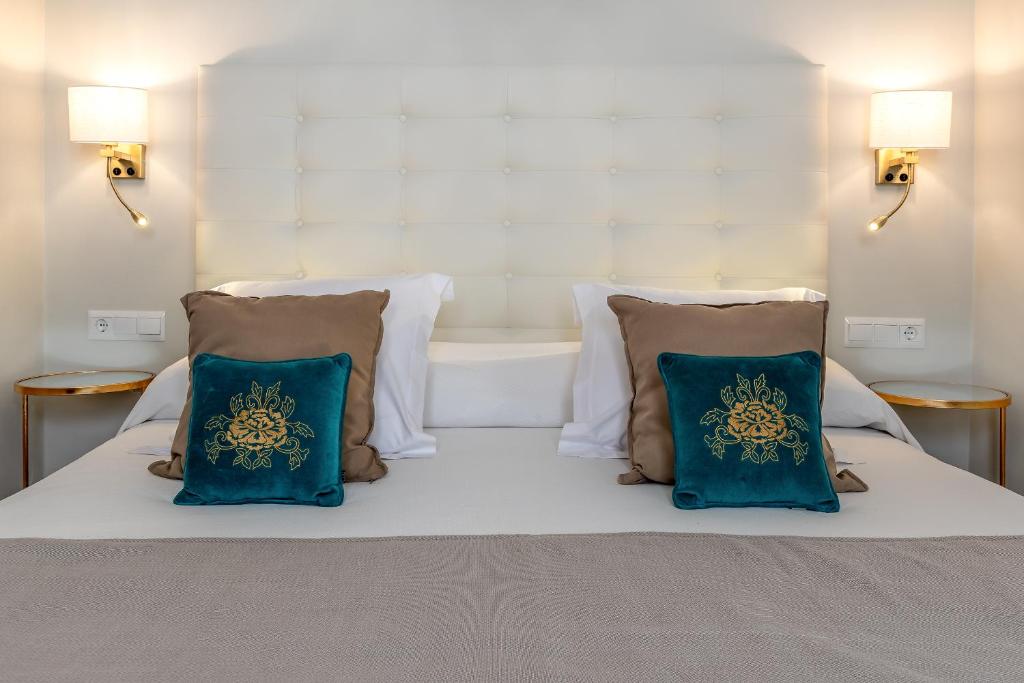 a white bed with two blue pillows on it at Hostal Boutique Plaza Cantarero in Nerja
