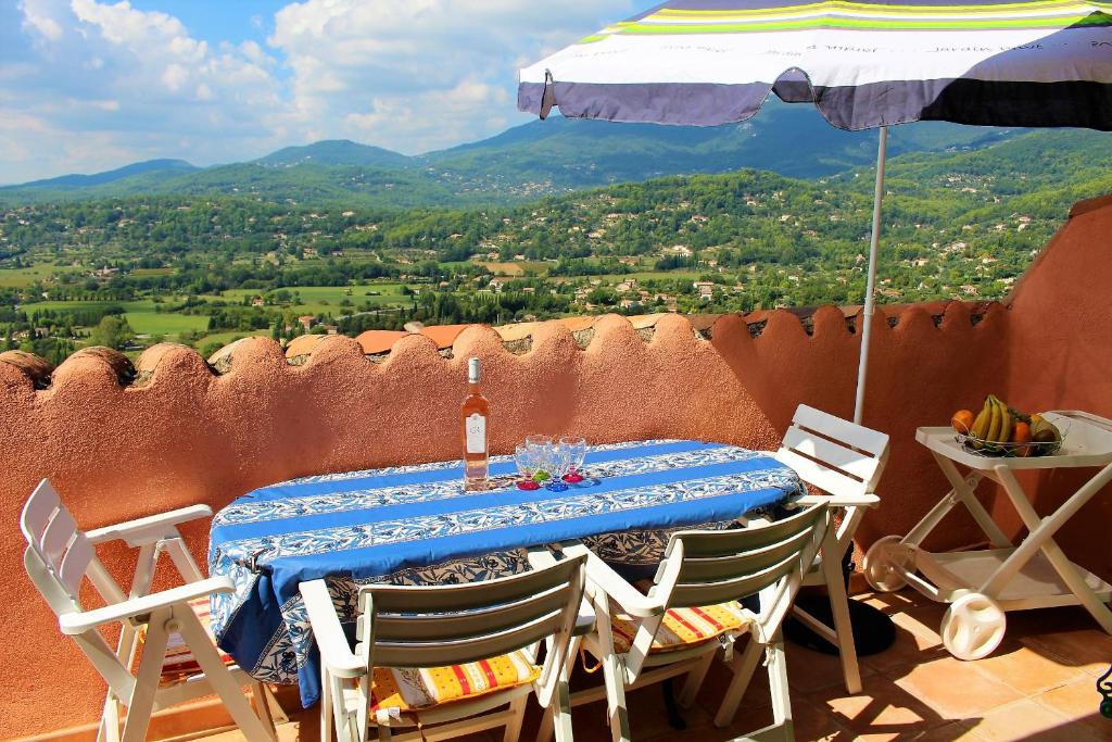 uma mesa com cadeiras e um guarda-sol numa varanda em Au bon accueil em Fayence