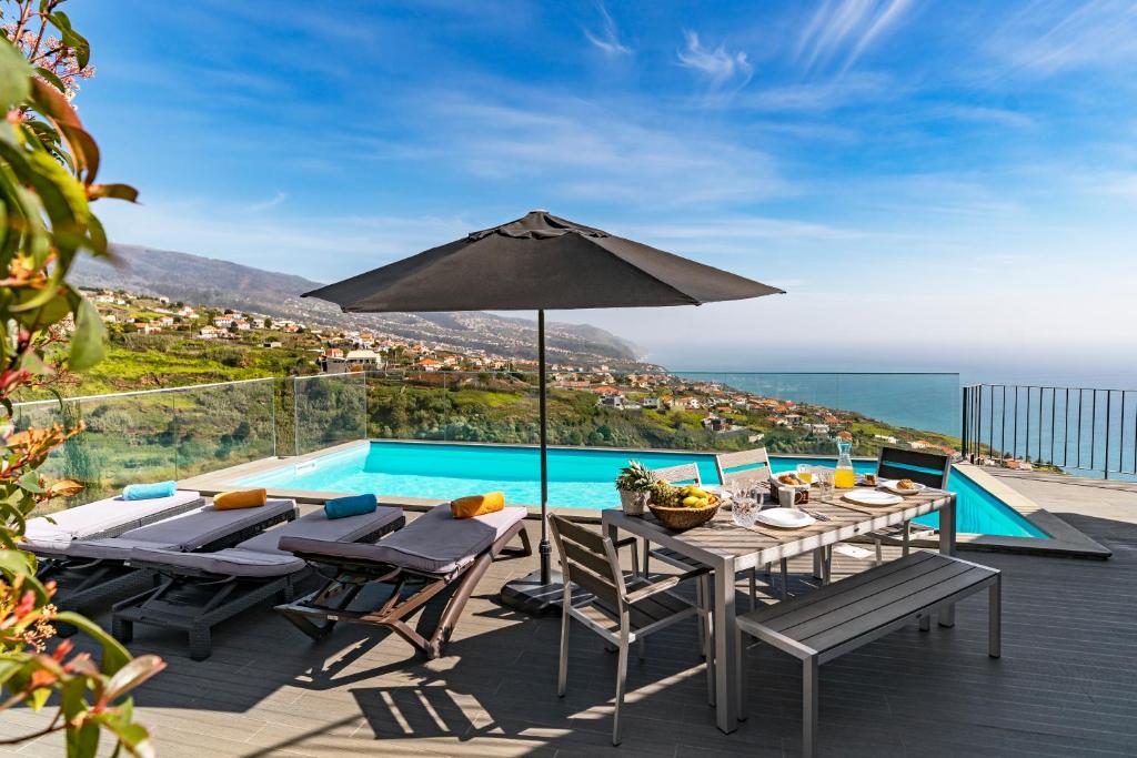 eine Terrasse mit einem Tisch mit einem Sonnenschirm und einem Pool in der Unterkunft Villa Clementina | Cliffs&Ocean | Heated Pool in Prazeres