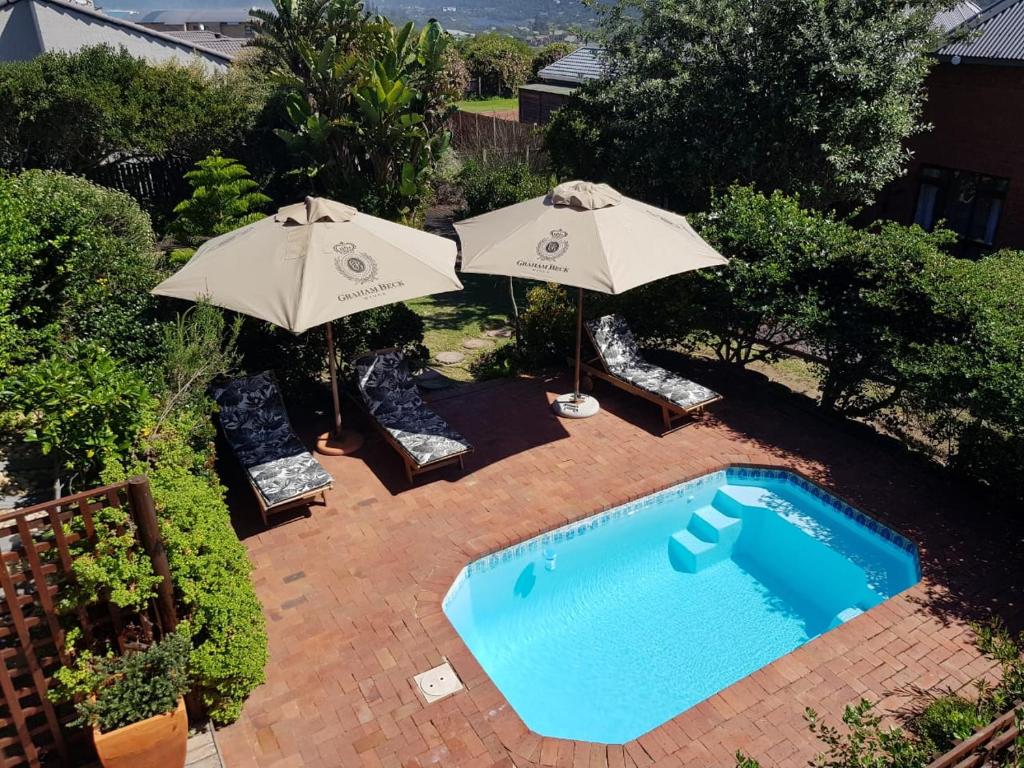 a swimming pool with two umbrellas and chairs next to at Dolphin Dunes Guesthouse in Wilderness
