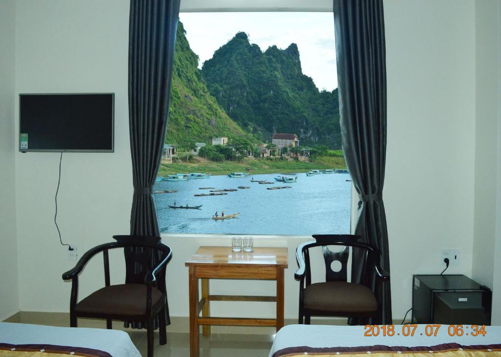 Zimmer mit 2 Stühlen und einem Fenster mit Booten im Wasser in der Unterkunft Son Doong Riverside in Phong Nha