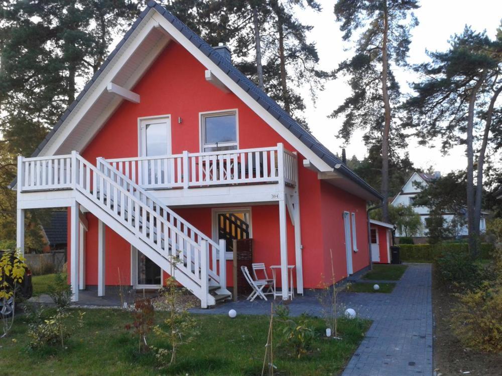 uma casa vermelha com um deque branco e escadas em K 104 OG - stilvolle Ferienwohnung am See mit Balkon & Sauna in Röbel an der Müritz em Marienfelde