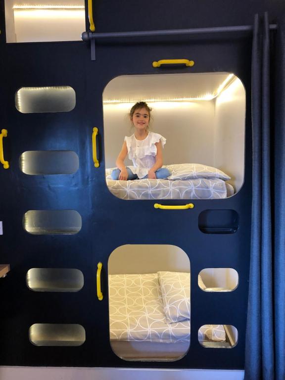 une jeune fille assise sur un lit superposé dans un bus dans l'établissement Willow Court Farm Studio South & Petting Farm, 8 mins from Legoland & Windsor, 15 mins from Lapland UK, à Windsor