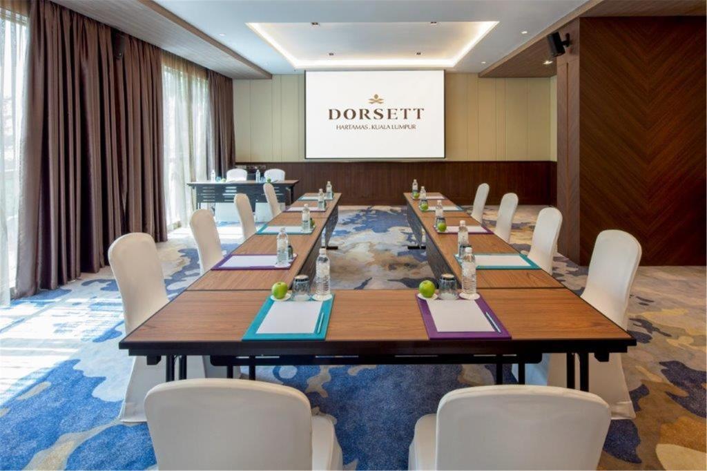 A dressed conference room with a long boardroom-style table and white-covered chairs.