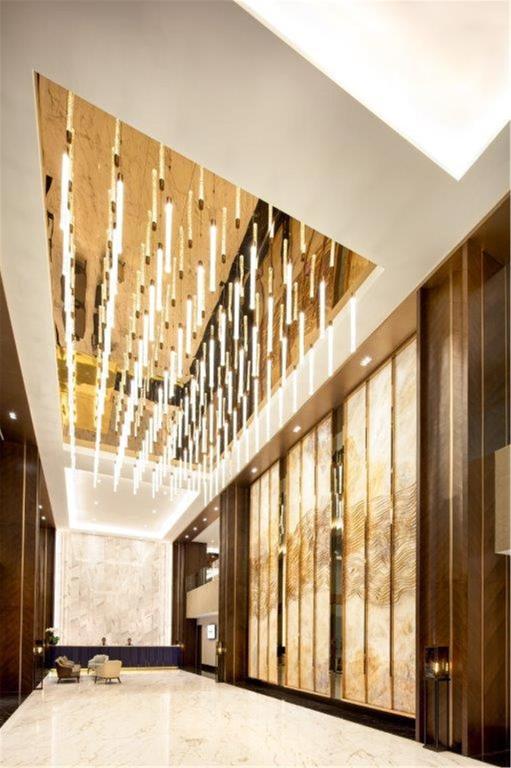 A tall hotel lobby with a dramatic suspended light installation and illuminated wall panels.