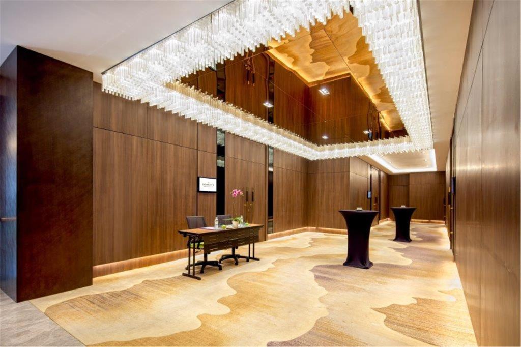 A wood-paneled function lobby with a large crystal-style chandelier and cocktail tables.