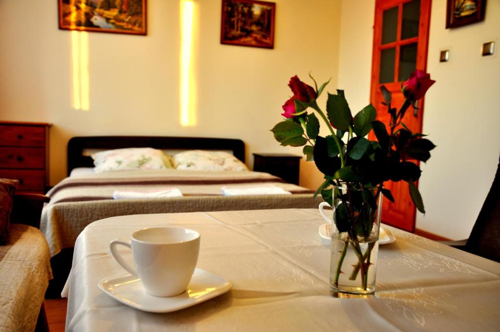 una mesa con un jarrón de rosas y una taza de café en Pokoje Sylwia z aneksami kuchennymi w każdym pokoju, en Ustroń