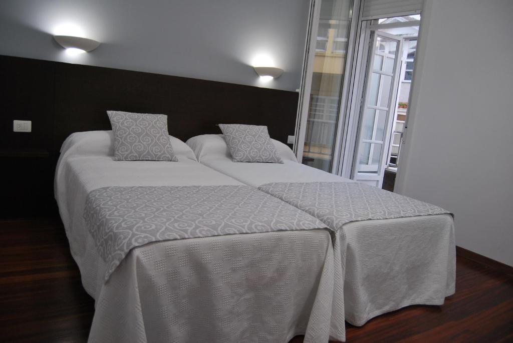 una camera con 2 letti con lenzuola e cuscini bianchi di Pensión Elisardo a Noya