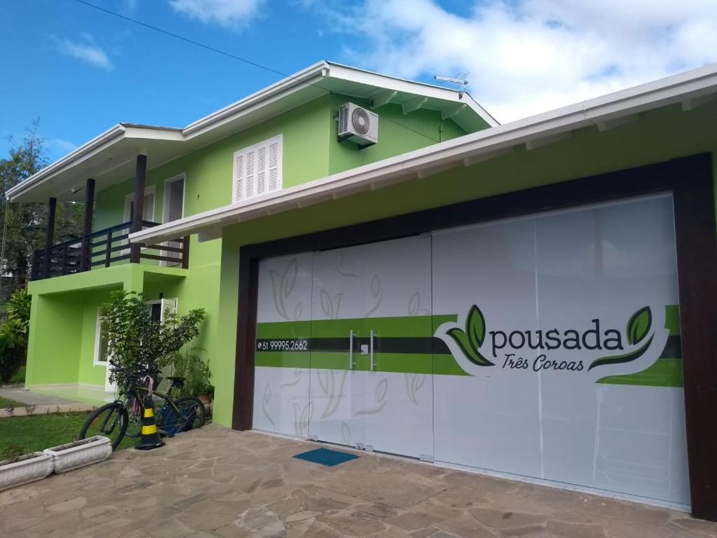 una casa verde con una puerta de garaje blanca en Pousada Três Coroas, en Três Coroas