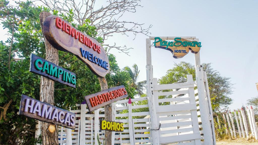 Ein Haufen Schilder an einem weißen Zaun in der Unterkunft Playa Samara Hostel in Camarones