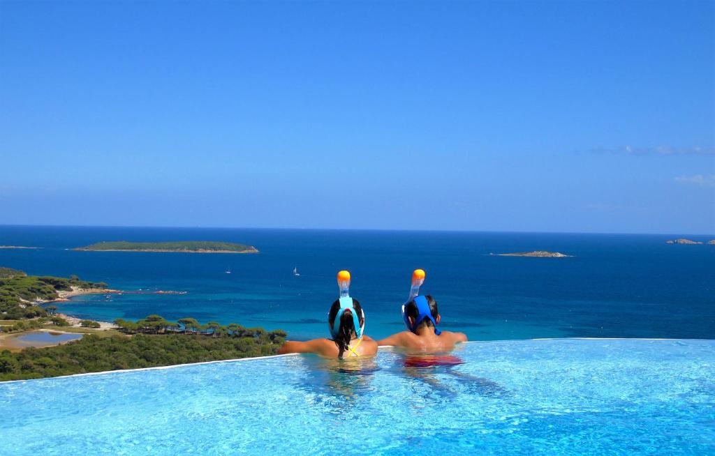 duas pessoas numa piscina com o oceano ao fundo em Résidence Belvedere de Palombaggia em Porto-Vecchio