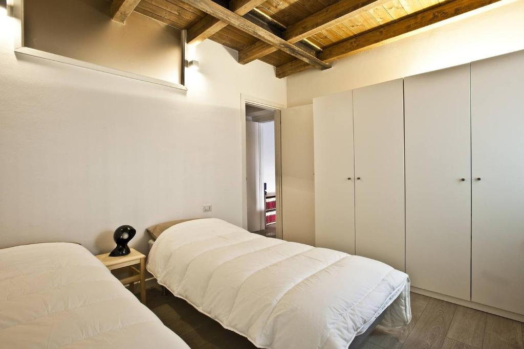 2 Betten in einem Zimmer mit weißen Wänden und Holzdecken in der Unterkunft CaseOspitali - CASA CARAMELLI bilocale in corte storica in Cernusco sul Naviglio