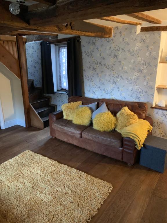 uma sala de estar com um sofá castanho com almofadas amarelas em The griffin cottage em Ludlow