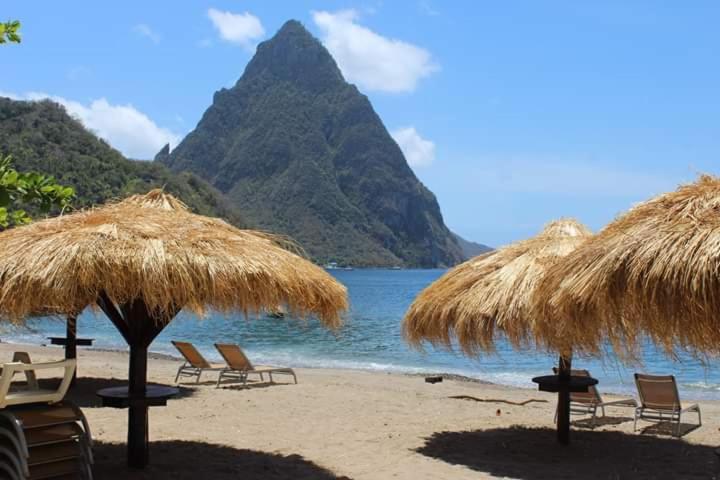 a beach with chairs and straw umbrellas and a mountain at Apartment Soleil- Because Location really is everything! in Soufrière