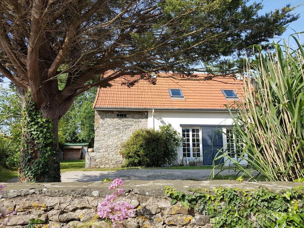 a house with a tree and a stone wall at La Casa Céline in Surtainville