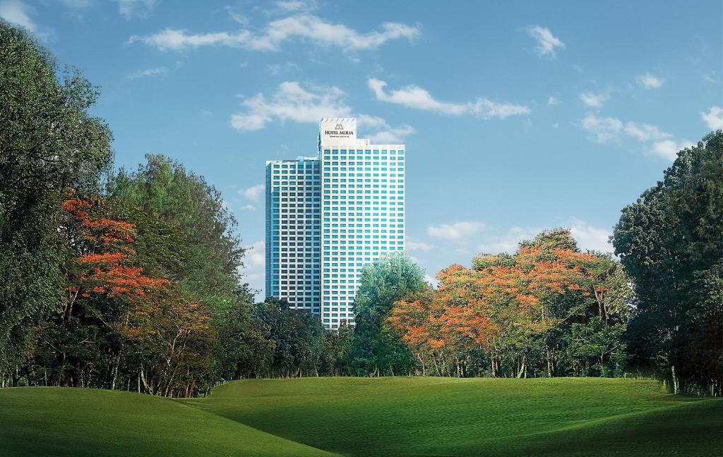 Hotel Mulia Senayan, Jakarta في جاكرتا: مبنى طويل في وسط حديقة فيها اشجار