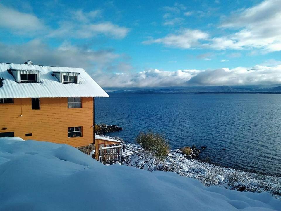 una casa en la nieve junto a un cuerpo de agua en Berkana hostel Bariloche en San Carlos de Bariloche