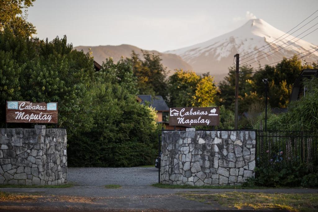 two signs on a stone wall with a mountain in the background at Cabañas Mapulay in Pucón