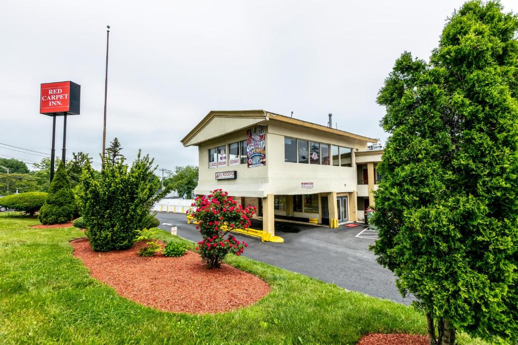 a building with flowers in front of a parking lot at Red Carpet Inn - Stamford in Stamford