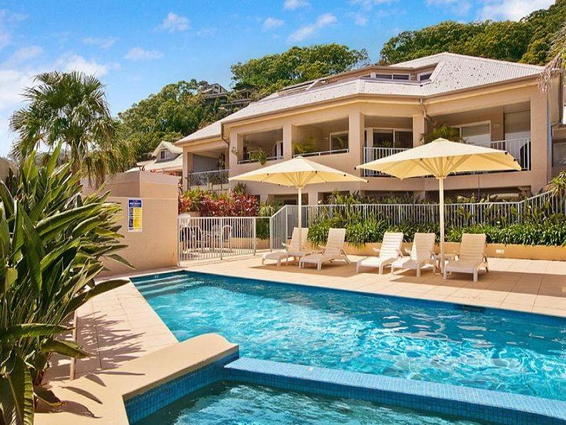 a house with a swimming pool with chairs and umbrellas at Iluka Resort Apartments Palm Beach in Palm Beach