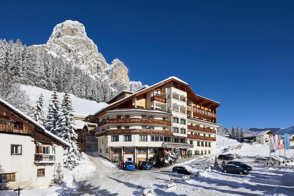 a large building in the snow in front of a mountain at Hotel Sassongher in Corvara in Badia