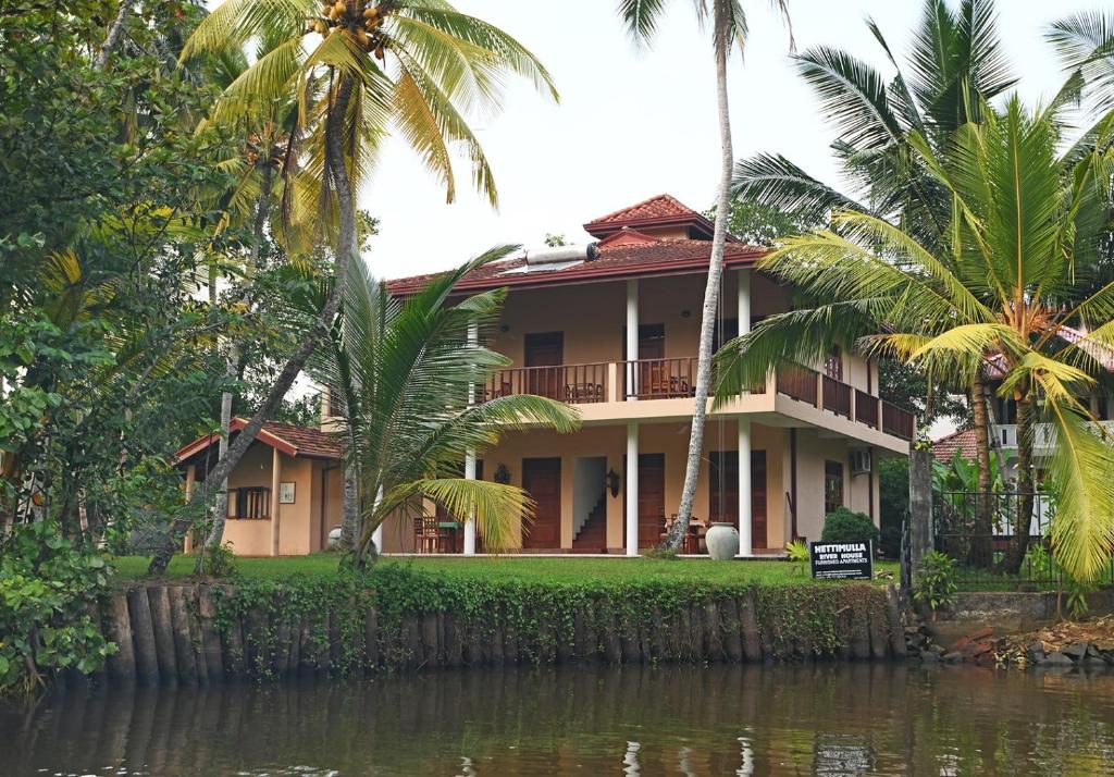 a house with palm trees in front of a body of water at Hettimulla River House in Bentota