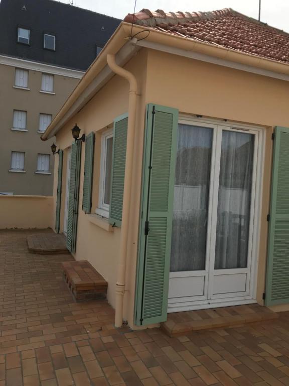 ein Haus mit grünen Rollläden auf einer Terrasse in der Unterkunft Riva Bella in Ouistreham