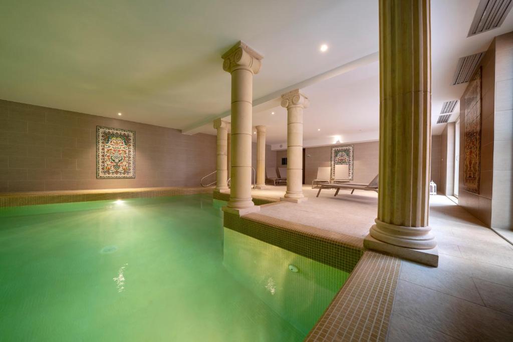 una piscina cubierta con columnas y agua verde en un edificio en Hotel Majestic Alsace - Strasbourg Nord, en Niederbronn-les-Bains