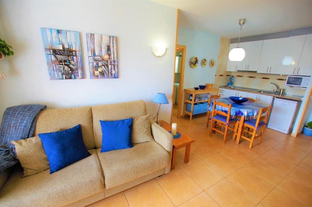 ein Wohnzimmer mit einem Sofa und einem Tisch sowie eine Küche in der Unterkunft V&V LLORET - APARTAMENTO BLAU precioso apartamento con piscina comunitaria, parking y aire acondicionado Solo se aceptan familias in Lloret de Mar