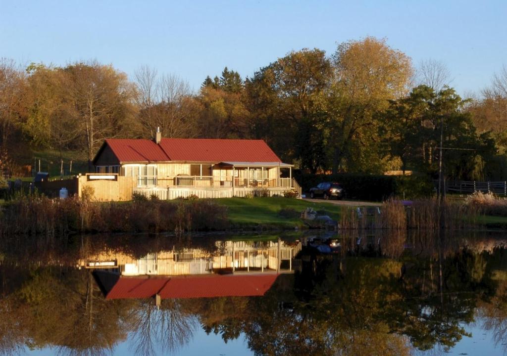 dom z czerwonym dachem siedzący obok jeziora w obiekcie Liftlock Guest House w mieście Peterborough